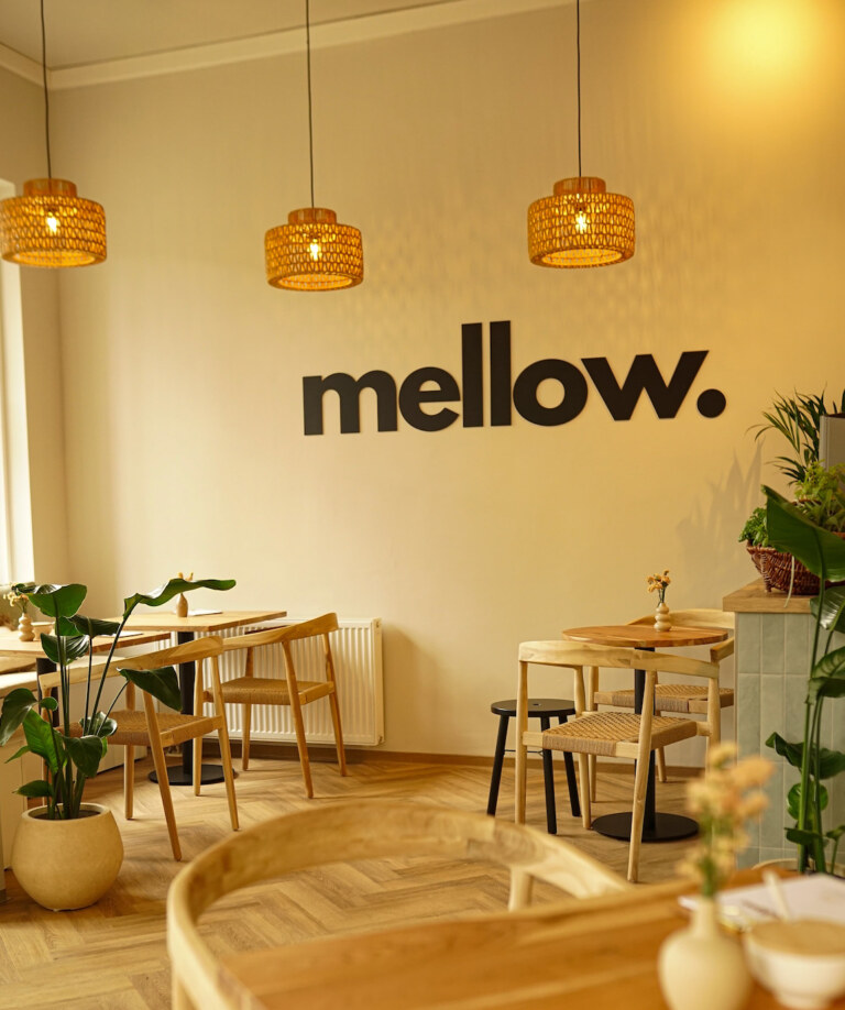 Innenraum des mellow. in Neubrandenburg mit Logo an der Wand, Holztischen und Hängelampen